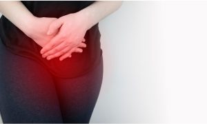 woman standing with her hands over her pelvis suffering from uterine fibroids symptoms