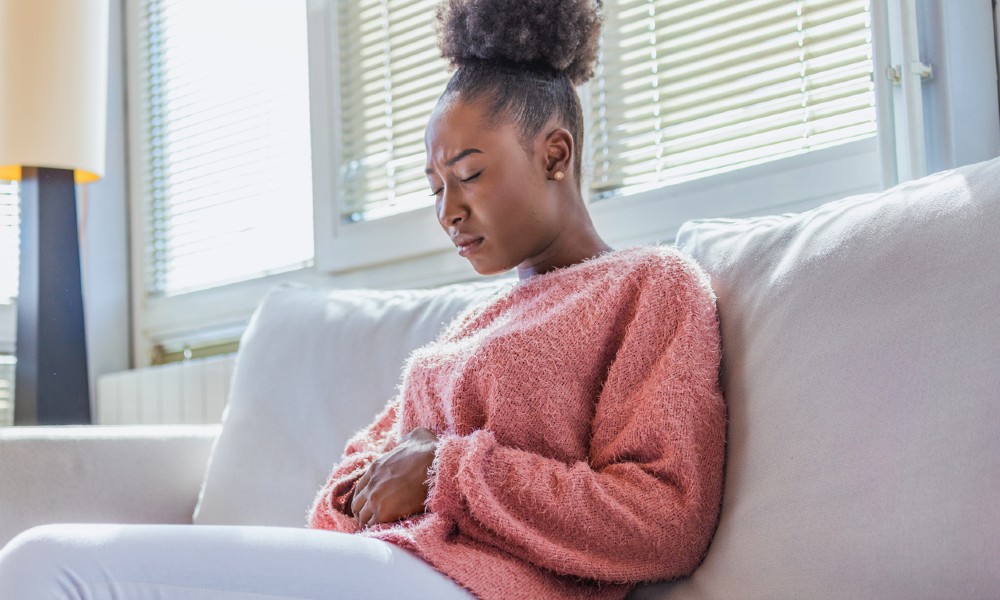 A woman sitting on a couch suffering from abdominal pain needs treatment for uterine fibroids.